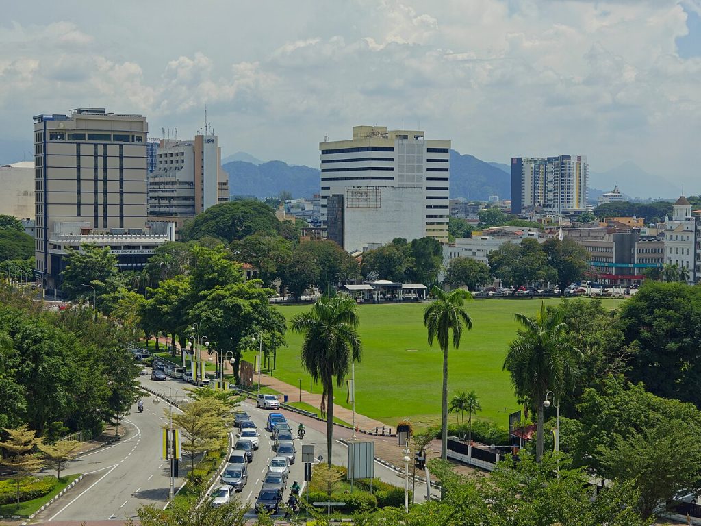Ipoh city skyline with high-rise buildings overlooking a green padang field and traffic-lined street, Perak, Malaysia
